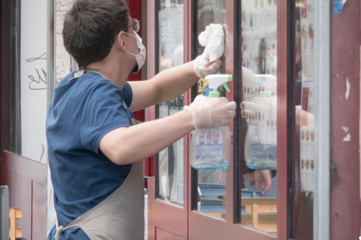 A man in gloves and a mask cleans a window, ensuring a clear view and maintaining hygiene during the task.